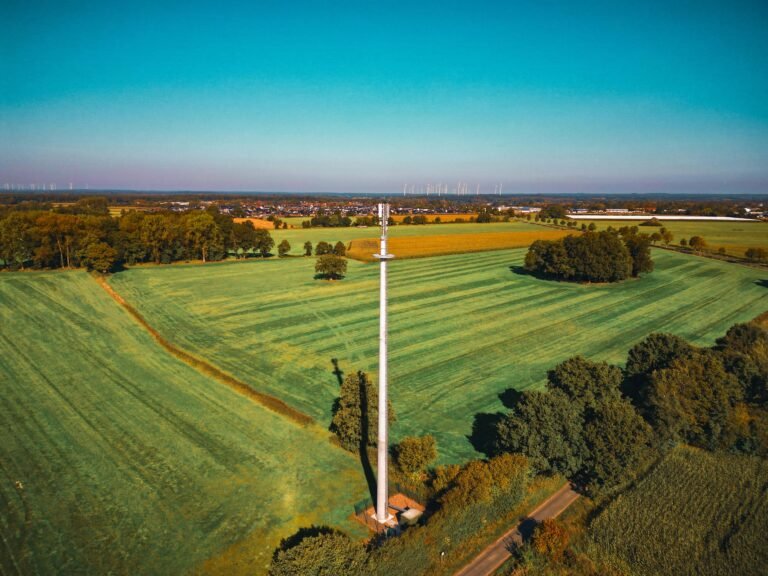 Aerial view showing a communication tower amidst expansive green fields under a clear blue sky.